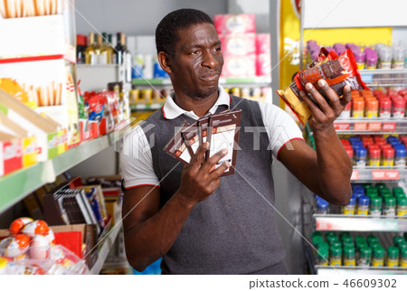 African man holding chocolate sweets packs in supermarket 46609302