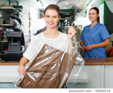Portrait of happy young woman in modern dry cleaning with clean clothes in plastic garment bag 46609558