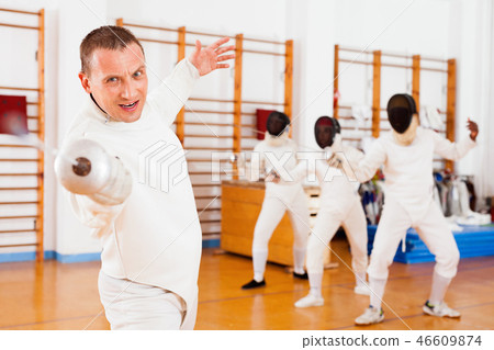 Sporty young man fencer practicing effective fencing techniques in training room Sporty young man fencer practicing effective fencing techniques in training room 46609874