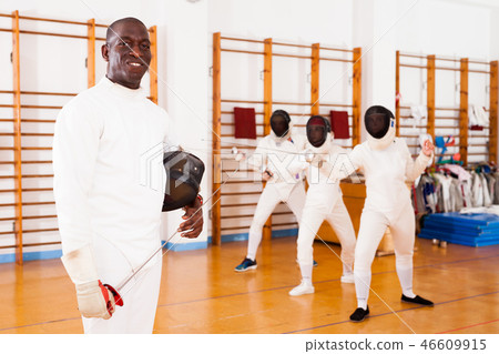 African american male fencer in uniform standing with mask and foil African american male fencer in uniform standing with mask and foil 46609915
