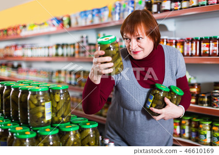 Adult female customer holding glass jar of cucumbers in the supermarket Adult female customer holding glass jar of cucumbers in the supermarket 46610169
