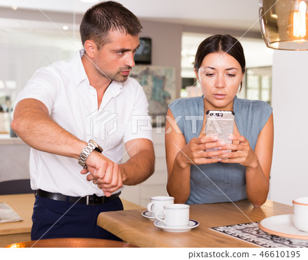 Annoyed man pointing at watch to girlfriend with phone Annoyed man pointing at watch to girlfriend with phone 46610195