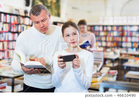Father trying to draw daughter attention to book while she carried away with phone Father trying to draw daughter attention to book while she carried away with phone 46610490