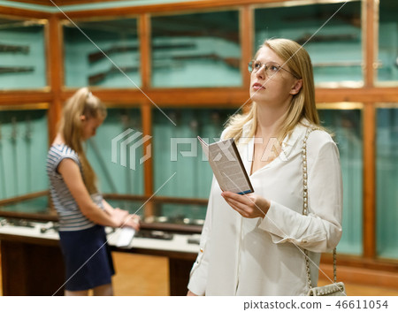 Woman holding guidebook in museum of art, girl on background Woman holding guidebook in museum of art, girl on background 46611054