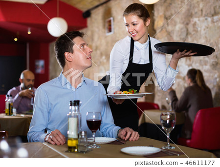 Polite waitress serving ordered dishes to smiling man at restaurant Polite waitress serving ordered dishes to smiling man at restaurant 46611177
