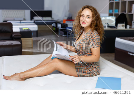 Young attractive woman choosing right mattress with booklet in home furnishings store Young attractive woman choosing right mattress with booklet in home furnishings store 46611291