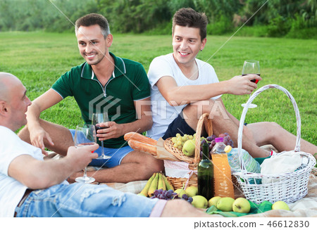 Three adult men enjoying picnic outdoors on summer day 46612830