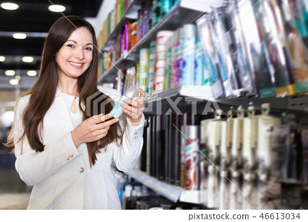 Smiling young female choosing haircare spray and other products at the shop 46613034