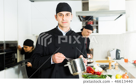 Portrait of man cook who is standing with pot for soup on his work place in the kitchen Portrait of man cook who is standing with pot for soup on his work place in the kitchen 46613440