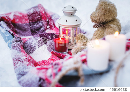 A close-up of a teddy bear with Christmas candles on a cozy checkered rug in the outdoors next to a 46616688