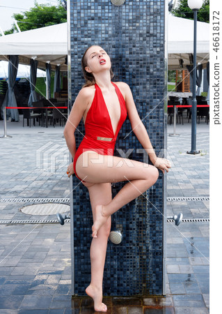 Beautiful young girl in red swimsuit near the pool takes a shower. sexy blonde girl with wet hair Beautiful young girl in red swimsuit near the pool takes a shower. sexy blonde girl with wet hair 46618172