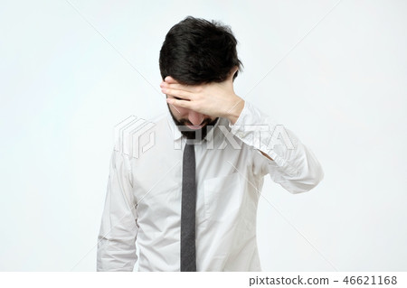 Exhausted young man covering face with hand while standing against grey background 46621168