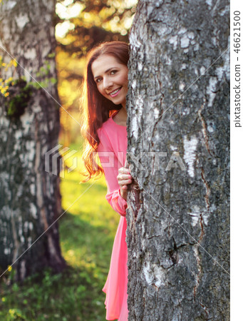 Young woman in pink dress, peek a boo behind tree Young woman in pink dress, peek a boo behind tree 46621500