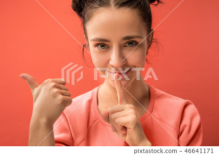 The young woman whispering a secret behind her hand over coral background The young woman whispering a secret behind her hand over coral background 46641171