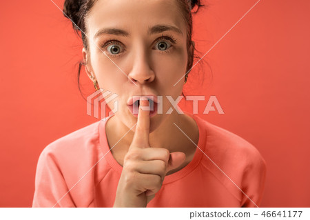 The young woman whispering a secret behind her hand over coral background The young woman whispering a secret behind her hand over coral background 46641177