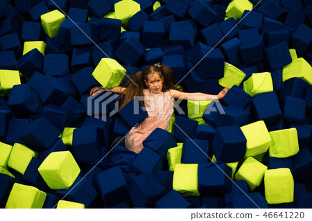 Little girl having fun in a dry pool with bright soft cubes to jump into. Kids playing room Little girl having fun in a dry pool with bright soft cubes to jump into. Kids playing room 46641220