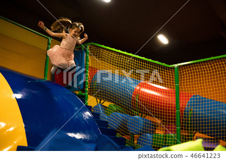 Little girl is jumping in the dry pool with bright soft cubes for play in kids play room Little girl is jumping in the dry pool with bright soft cubes for play in kids play room 46641223
