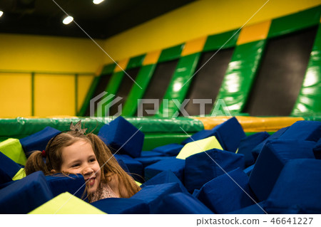 Little girl having fun in a dry pool with bright soft cubes to jump into. Kids playing room Little girl having fun in a dry pool with bright soft cubes to jump into. Kids playing room 46641227