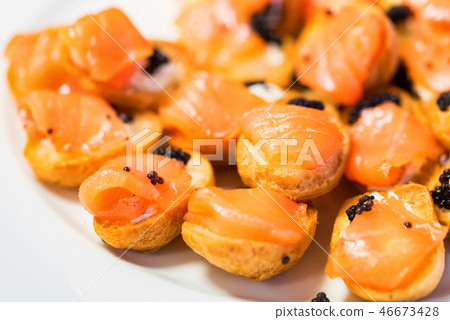 Delicious profiteroles with black caviar and salmon on a plate close-up Delicious profiteroles with black caviar and salmon on a plate close-up 46673428