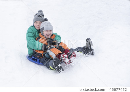 Two joyful boys slides down hill on snow saucer Two joyful boys slides down hill on snow saucer 46677452
