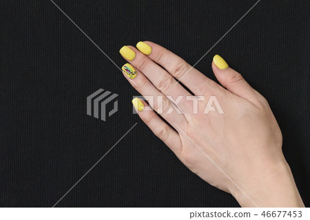 Female hand with yellow manicure on black fabric Female hand with yellow manicure on black fabric 46677453