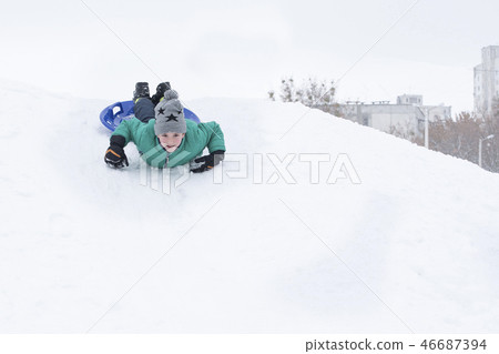 Laughing boy rides on his stomach from a hill Laughing boy rides on his stomach from a hill 46687394
