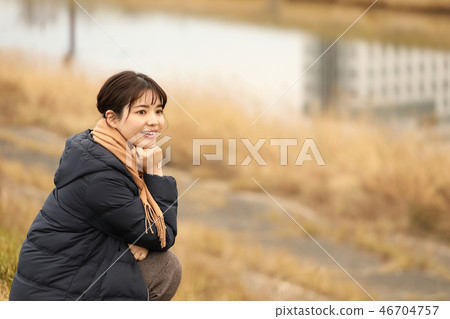 A woman squatting on a dike and looking at a distance 46704757