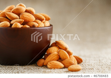 Almonds in a wooden cup on a burlap cloth background. Almonds in a wooden cup on a burlap cloth background. 46708483