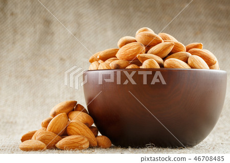 Almonds in a wooden cup on a burlap cloth background. 46708485