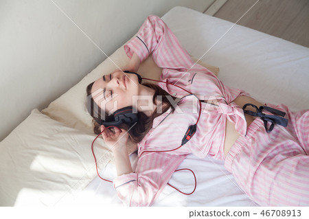 woman in pink Pajamas listening to music in headphones dancing on the bed 46708913