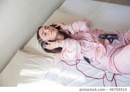 woman in pink Pajamas listening to music in headphones dancing on the bed woman in pink Pajamas listening to music in headphones dancing on the bed 46708918