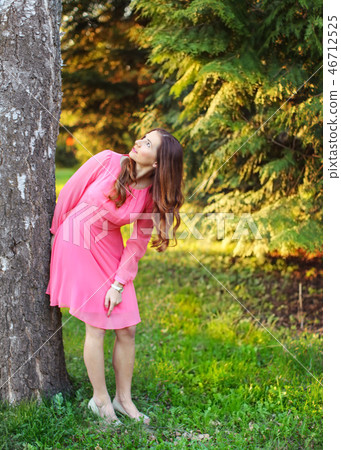 Young woman in pink dress, at tree, looking up 46712525