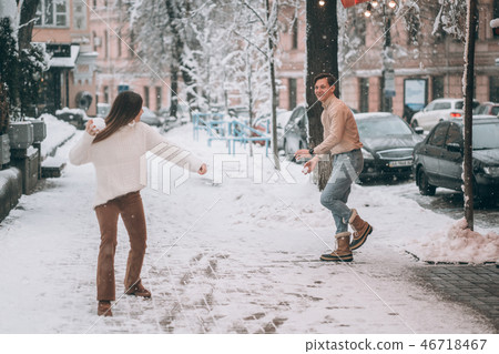 Joyful young couple in sweaters is playing snowballs at the street. Joyful young couple in sweaters is playing snowballs at the street. 46718467