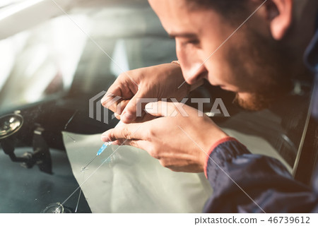 Close-up of a professional windshield repairman fills a crack in the glass with a special polymer Close-up of a professional windshield repairman fills a crack in the glass with a special polymer 46739612