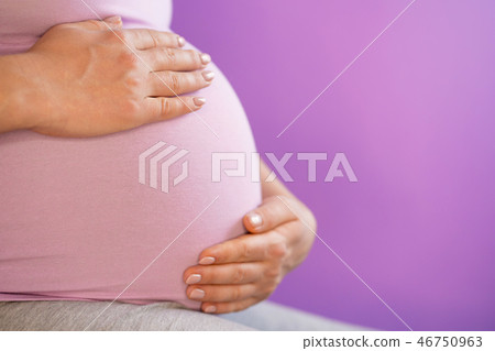 Pregnant woman holding her hands on tummy belly. Young girl expecting baby on pink bakcground 46750963