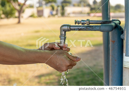 Man washing hands from plumbing tap outdoor. 46754931