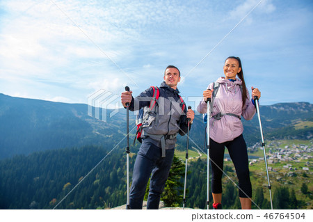 Hikers with backpacks relaxing on top of a mountain and enjoying the view of valley Hikers with backpacks relaxing on top of a mountain and enjoying the view of valley 46764504