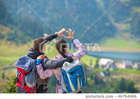 Two hikers at viewpoint in the mountains enjoying beautiful view of the valley with a lake. Two hikers at viewpoint in the mountains enjoying beautiful view of the valley with a lake. 46764906