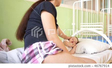 child sleeps in the hospital ward on white bed under the supervision of mom. mother measures 46767914