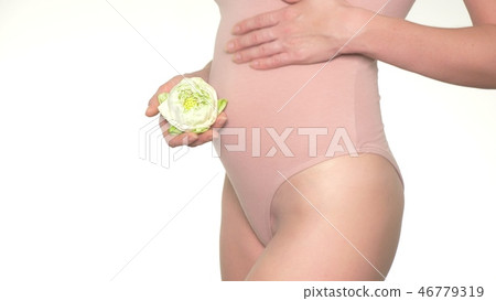 Close-up of a pregnant woman holding a white lotus flower next to her belly 46779319