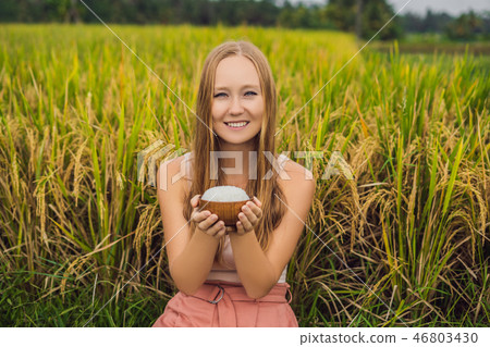 A woman is holding a cup of boiled rice in a wooden cup on the background of a ripe rice field 46803430