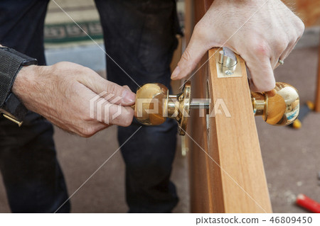 Carpenter installs handle with lock in door leaf. 46809450
