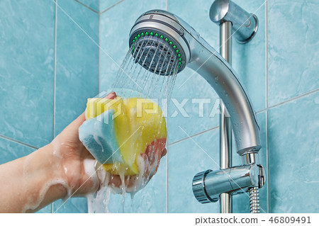 Wet sponge in human hand under shower head 46809491