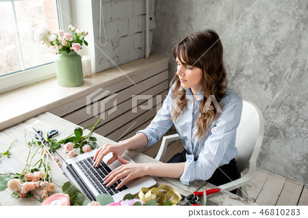 Young friendly smiling woman florist create ordering in the working base on a laptop. Flower 46810283