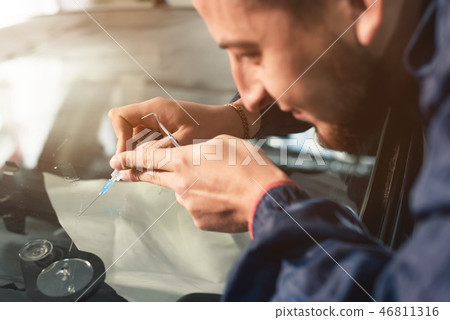 Close-up of a professional windshield repairman fills a crack in the glass with a special polymer 46811316