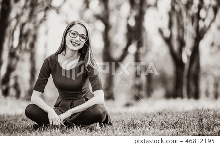 Young woman sitting on a lawn in a park Young woman sitting on a lawn in a park 46812195