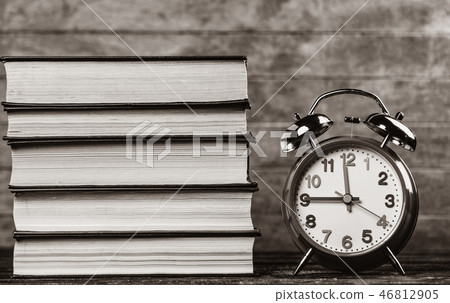 Alarm clock and books on wooden table. 46812905