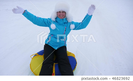 beautiful young woman slides slide in snow on an inflatable snow tube and waves hand. Happy girl beautiful young woman slides slide in snow on an inflatable snow tube and waves hand. Happy girl 46823692
