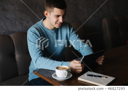 Man is sitting in a cafe and using a tablet. Student spend time in cafe and drink coffee. He study Man is sitting in a cafe and using a tablet. Student spend time in cafe and drink coffee. He study 46827293
