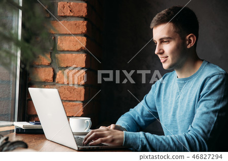 Young programmer with laptop in a cafe sits opposite the window Young programmer with laptop in a cafe sits opposite the window 46827294